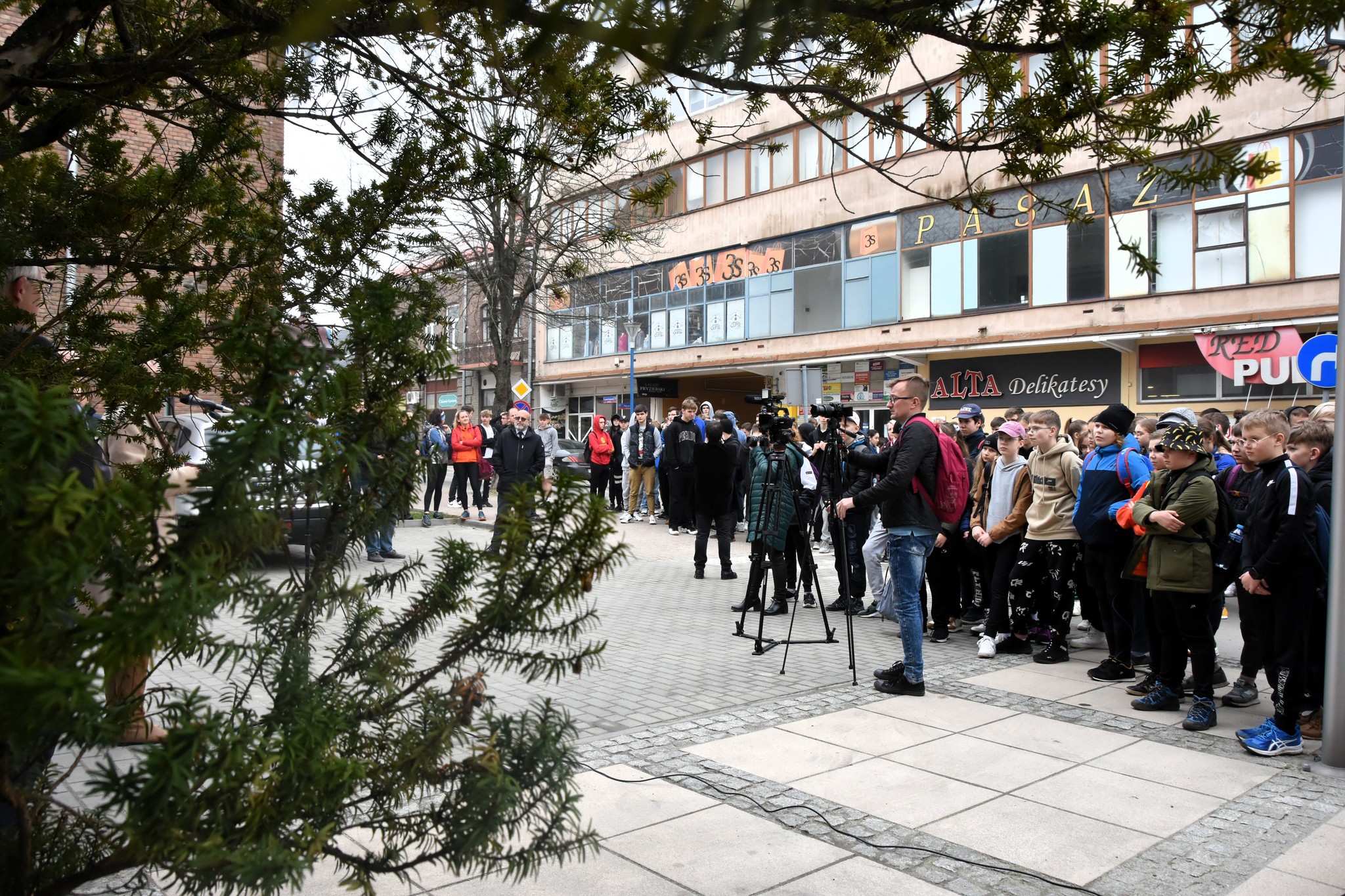 Grupa młodzieży stoi na placu przed urzędem w centrum miasta.