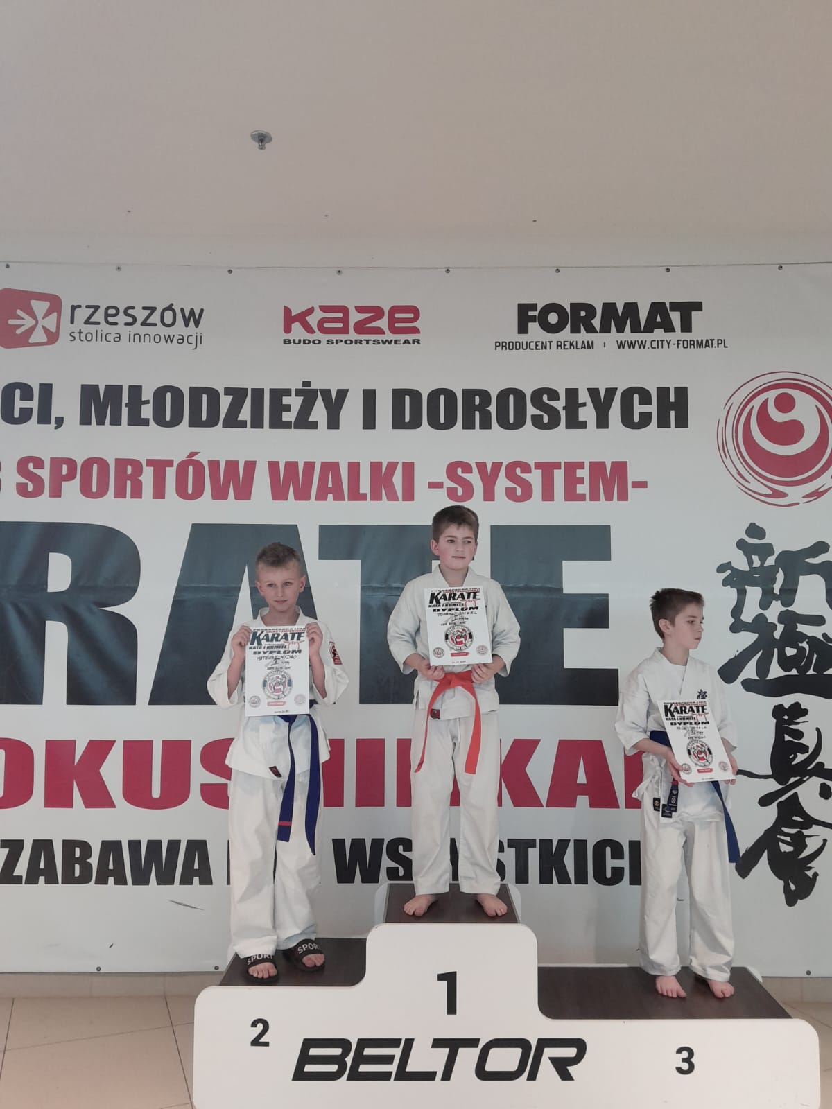 Grupa chłopców w wieku szkolnym stoi na podium w w kimonach koloru białego.