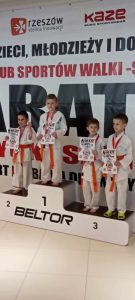 Grupa chłopców w wieku szkolnym stoi na podium w w kimonach koloru białego.