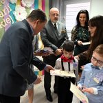 Mężczyzna w średnim wieku wręcza dzieciom i Paniom opiekunkom dyplomy i nagrody.