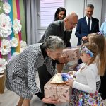 Kobieta w średnim wieku wręcza dzieciom i Paniom opiekunkom dyplomy i nagrody.